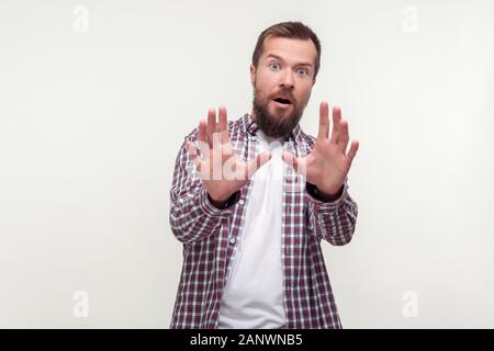 Portrait of frightened shocked bearded man in casual plaid shirt standing with scared eyes and arms raised trying to defend himself, panic attack. ind Stock Photo
