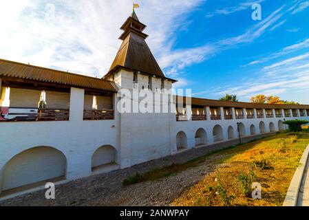 White stone wall of the courtyard with large arches and a wooden roof along the road with masonry in cloudy weather with blue clouds. Historical and a Stock Photo