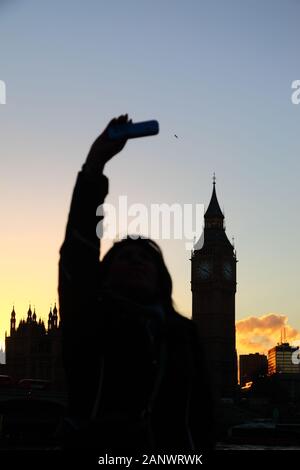 Silhouette of girl taking selfie with Big Ben in background at sunset, South Bank, London, England. Focus on Big Ben. Stock Photo