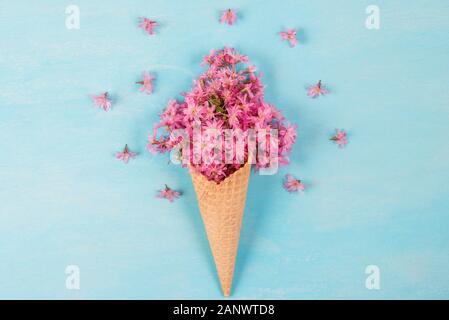 Ice cream cone with spring blossom pink cherry or sakura flowers on blue background. Minimal spring concept. Flat lay. top view Stock Photo