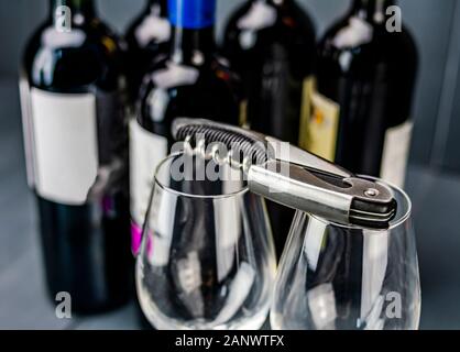 Traditional corkscrew on glass wine glasses and bottles of red wine in the background ready to be opened and tasted Stock Photo