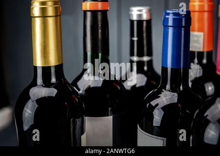 Bottles of red wine grouped with labels of different colors in the foreground on gray background Stock Photo