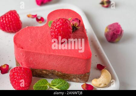 raw vegan raspberry heart shaped cake or cheesecake with fresh berries, nuts, mint and dried flowers. Valentines day dessert. close up Stock Photo