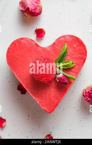 heart shaped raw vegan cake or cheesecake with fresh raspberries, mint and dried flowers. Valentines day dessert. healthy delicious food. top view. Ve Stock Photo