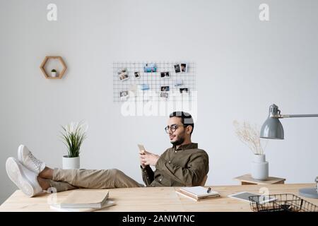 Young relaxed businessman in casualwear scrolling in mobile phone Stock Photo