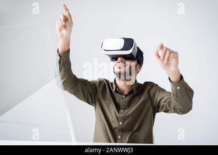 Young contemporary man in vr headset pointing at virtual display Stock Photo