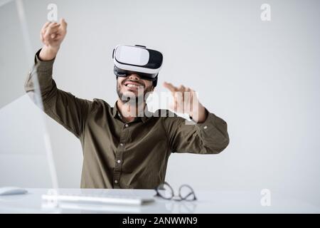 Young cheerful businessman in vr headset making presentation by workplace Stock Photo