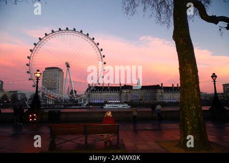 Woman sitting on seat on North Bank looking at London Eye, Shell Centre building and County Hall at sunset, London, England Stock Photo