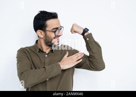 Smiling young strong man in eyeglasses and shirt touching his muscles Stock Photo