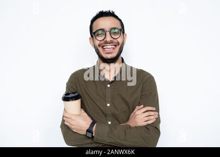 Laughing guy with glass of coffee crossing arms on chest against white wall Stock Photo
