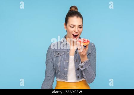 Delighted beautiful woman with hair bun looking at delicious doughnut with desire, keeping her mouth opened and dreaming to bite eat sweet donut, temp Stock Photo