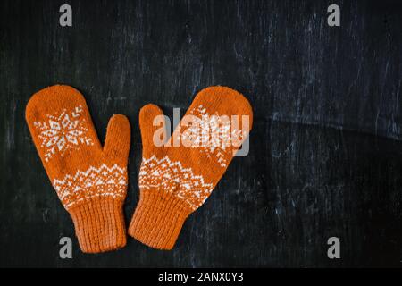 a pair of yellow orange knitted mittens on a dark blue-green-brown wooden Stock Photo