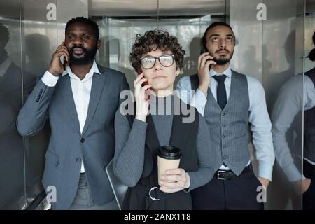Young intercultural business people calling by smartphones in elevator Stock Photo