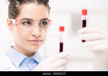Serious female clinician in protective eyeglasses looking at samples Stock Photo