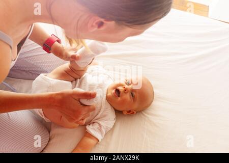 Young happy mother hold little infant baby boy holding legs playing in the bed view above Stock Photo