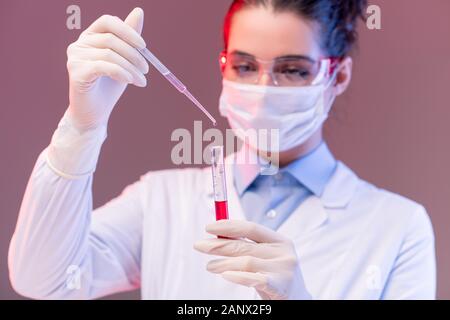 Young scientist dropping red liquid substance into flask while making experiment Stock Photo