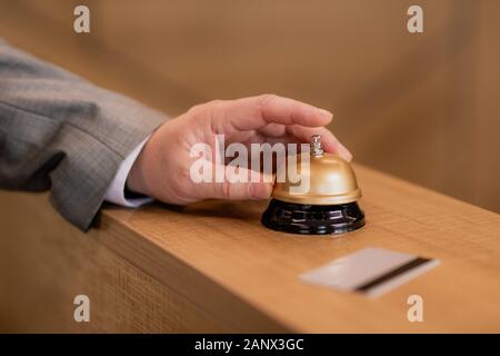 Hand of traveling businessman pushing ring button on wooden reception counter Stock Photo