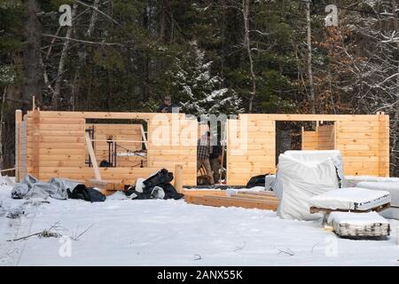 Three construction workers assembling a manufactured log home on a cold winter day in the snow in Speculator, NY USA Stock Photo