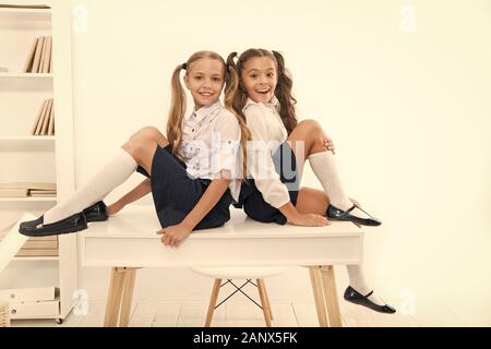 Rebellious spirit. School club. Little schoolgirls classmates friendly kids. Schoolgirls friends sit on desk. Best friends relaxing. Schoolgirls tidy hairstyle relaxing having rest. School uniform. Stock Photo