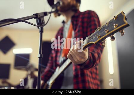 Close up of contemporary man holding guitar while singing to microphone during rehearsal or concert with music band, copy space Stock Photo