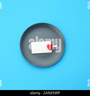 empty round gray plate and decorative red heart, next to an empty white business card, blue background Stock Photo
