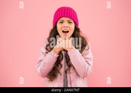 she has sore throat. cold climate weather. happy little girl pink background. kid puffer jacket and knitted hat. winter shopping. how to dress warm in winter. ready for cold winter. no flu. Stock Photo