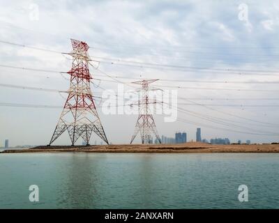 Red and white overhead electricity power lines and cables crossing water supported by large red and white pylons in Abu Dhabi, UAE Stock Photo