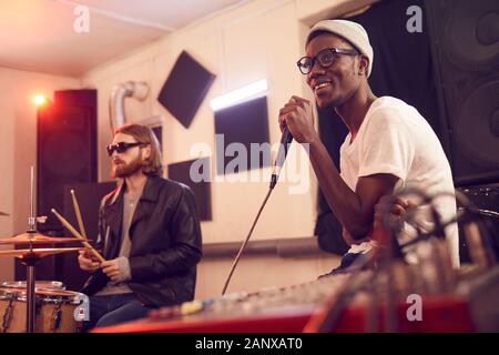 Portrait of contemporary African-American man singing to microphone and smiling happily during rehearsal or concert in music studio, copy space Stock Photo