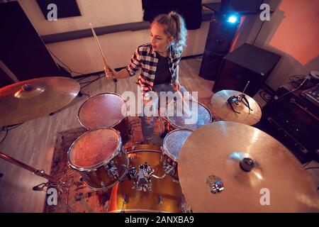 Above view portrait of young woman playing drums in recording studio lit by red lights, copy space Stock Photo