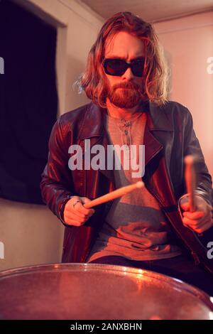 Waist up portrait of handsome young man rocking drums during music concert in bright lights Stock Photo