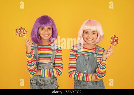 Anime cosplay party concept. Happy little girls. Anime fan. Kids with artificial hairstyles eating lollipops. Anime convention. Vibrant characters fantastical themes. Modern childhood. Childrens day. Stock Photo