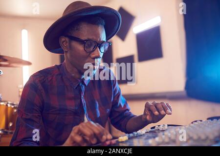 Portrait of contemporary African-American man writing music in recording studio using sound equalizing equipment, copy space Stock Photo
