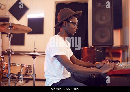 Side view portrait of young African-American man writing music in recording studio using sound equalizing mixer, copy space Stock Photo