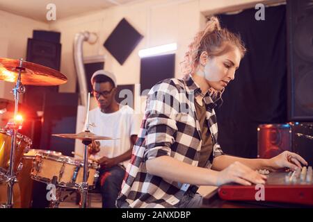 Portrait of contemporary band writing music in recording studio focus on young woman using sound mixer in foreground, copy space Stock Photo