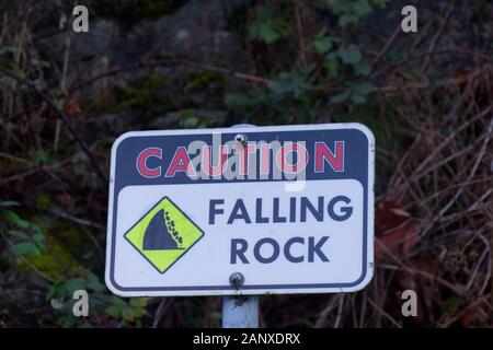Falling stone warning traffic sign on the road with bushes in the background. Stock Photo