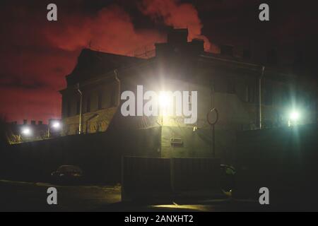 A night view of protected creepy penitentiary prison building facility, asylum exterior with barded wire on walls, red night sky, concept of scary hou Stock Photo