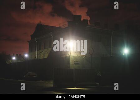 A night view of protected creepy penitentiary prison building facility, asylum exterior with barded wire on walls, red night sky, concept of scary hou Stock Photo