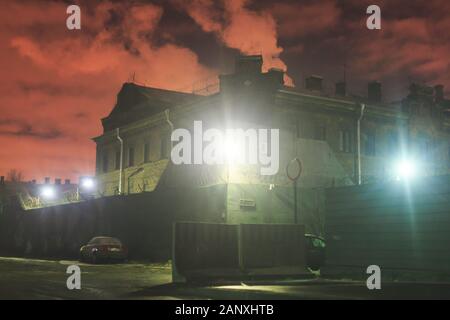 A night view of protected creepy penitentiary prison building facility, asylum exterior with barded wire on walls, red night sky, concept of scary hou Stock Photo