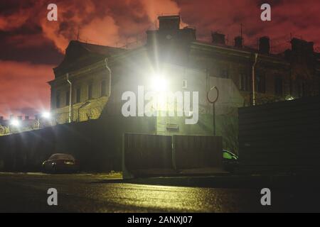 A night view of protected creepy penitentiary prison building facility, asylum exterior with barded wire on walls, red night sky, concept of scary hou Stock Photo