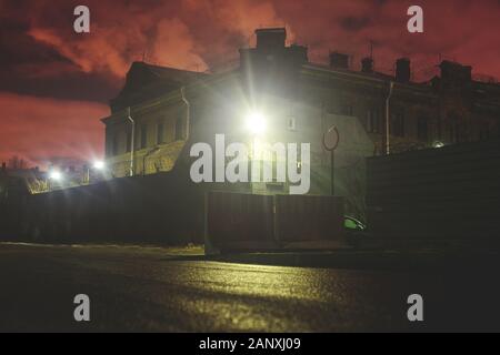 A night view of protected creepy penitentiary prison building facility, asylum exterior with barded wire on walls, red night sky, concept of scary hou Stock Photo