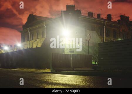 A night view of protected creepy penitentiary prison building facility, asylum exterior with barded wire on walls, red night sky, concept of scary hou Stock Photo