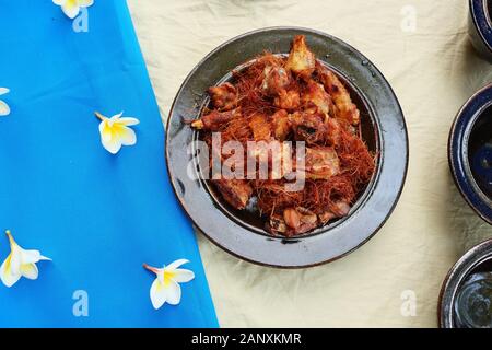 Deep fried chicken topped with lemongrass and galangal fries in a black dish, Cambodian food on table covered in white and blue cloths decorated Stock Photo