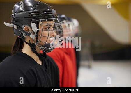 Side view portrait of female hockey team standing in line before match on rink, focus on beautiful woman wearing sports helmet in foreground, copy space Stock Photo