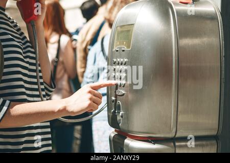 Close-up of a girl dialing a number or calling on a stationary street phone or from a telephone booth on a street in Italy. Stock Photo