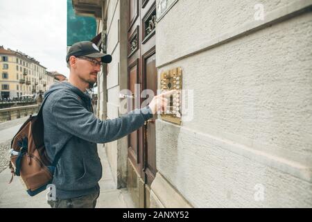 A guy or a man or a tourist presses a doorphone button to access inside. Stock Photo