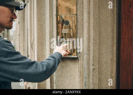 A guy or a man or a tourist presses a doorphone button to access inside. Stock Photo