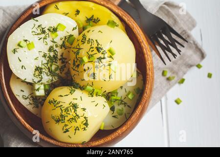 Boiled potatoes with greens in a wooden bowl, white wooden background. Stock Photo