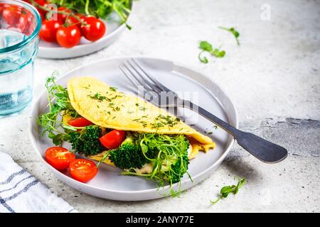 Vegan chickpea omelet with broccoli, tomatoes and seedlings on a gray plate. Healthy vegan food concept. Stock Photo