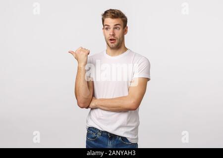 Astounded and impressed cute bearded blond caucasian male in t-shirt, pointing and looking left speechless, getting interested, attend good lecture Stock Photo