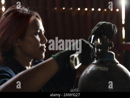 Female apprentice industrial engineer, inspecting and maintaining compressed gas cylinders in production plant - Trainee student intern, learning on the job skills during work experience Stock Photo